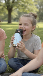Load image into Gallery viewer, Child holding a light blue insulated bamba kids drink bottle outdoors with greenery in the background
